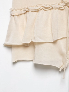 Détail d'un haut en tricot beige avec des volants superposés et des cordons ajustables