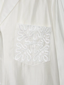 Detailed macro view of white satin shirt featuring intricate floral pocket embroidery