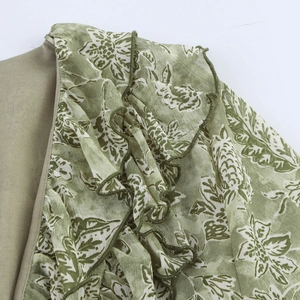 Détail de la robe patchwork vert sauge avec imprimé fleuri et volants sur l'épaule gauche