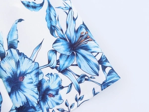 Close-up of blue lily floral print and fine stitching on white summer dress fabric