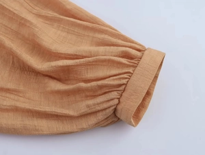 Dettaglio della manica di un abito estivo arancione con texture a pieghe e polsino