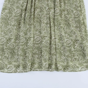 Détail de l'ourlet de la robe fleurie verte montrant l'imprimé vintage et le drapé