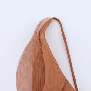 Détail du tissu mousseline plissé caramel avec une fine bretelle sur une robe d'été