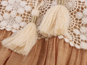 Dettaglio corpetto in pizzo all'uncinetto crema e tessuto a pieghe con nappe beige