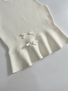 Détail d'un haut en maille sans manches crème avec nœuds décoratifs et ourlet à volants
