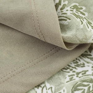Vue macro détaillée du tissu taupe avec imprimé feuilles vertes et ourlet à double couture