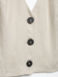 Detail of oatmeal linen vest showing natural fabric texture and three dark brown buttons