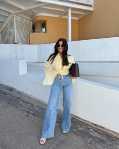 Detail of light yellow lace-up top with flared sleeves and high waist blue jeans
