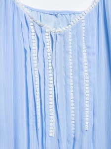 Detailed macro view of light blue vertical pleats and white lace embroidery on a dress
