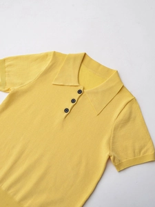 Detail of soft yellow knit Polo shirt featuring black buttons and ribbed sleeve texture