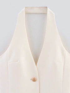 Detail of cream halter vest featuring a deep V-neck and decorative gold woven button