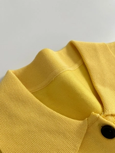 Close-up of yellow knit polo collar showing fine texture and a single black button