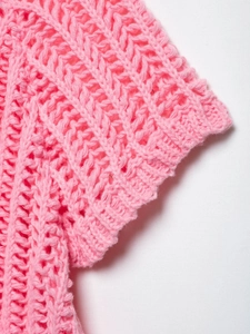 Détail du haut en tricot rose montrant la texture ajourée et les poignets côtelés