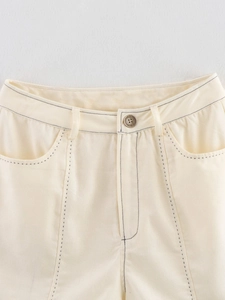 Détail d'un pantalon crème taille haute avec surpiqûres sombres contrastées et bouton