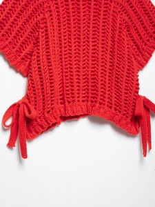 Détail de haut en maille crochet rouge avec laçage latéral et nœuds décoratifs