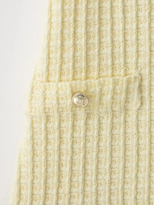 Detail view of cream knit dress featuring vertical texture and a gold crest button