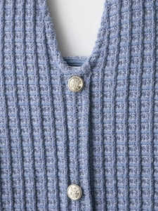 Détail de maille gaufrée bleu clair et boutons métalliques dorés à relief vintage