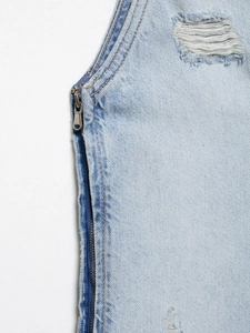 Detailansicht eines Jeanskleides in Hellblau mit silbernem Reißverschluss und Destroyed-Effekten