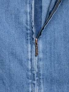 Close-up detail of vintage bronze zipper and stitching on washed blue denim dress