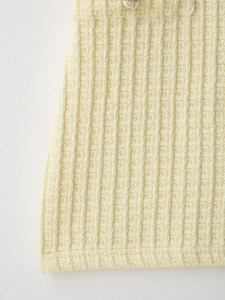 Macro detail of ribbed knit fabric in cream yellow with decorative gold crest button