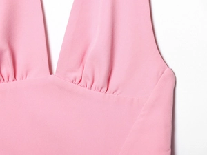 Detail of pink dress featuring a deep V-neckline, halter neck design, and pleated empire waist