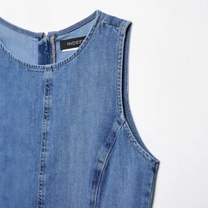 Blue sleeveless denim dress with round neck and detailed stitching from a side angle
