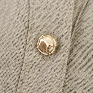 Macro detail of irregular gold metal buttons on beige linen fabric dress with textures