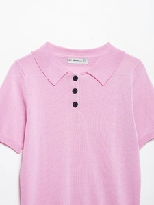 Détail du col d'un polo en maille rose avec trois boutons noirs et étiquette de marque