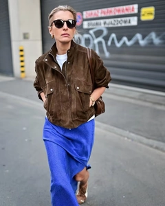 Street style shot of a brown suede jacket with pockets and a blue midi skirt on city streets