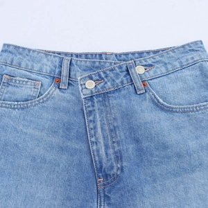 Detail of high waist denim jeans featuring asymmetric crossover waist and silver buttons