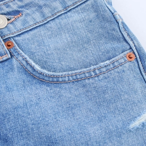 Detailed close-up of light blue denim fabric with orange stitching and copper rivets