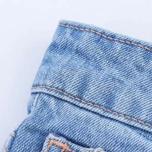Detailed close-up of light blue denim fabric featuring orange double stitching lines