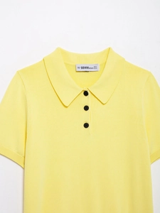 Gros plan détaillé du col polo en tricot jaune avec boutons noirs et étiquette tissée blanche