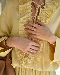 Macro di un set di gioielli dorati minimalisti con camicia in chiffon giallo