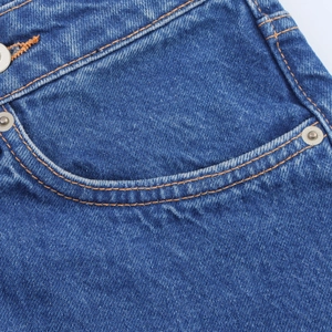 Detail of blue denim jeans with orange double stitching and silver metal rivets
