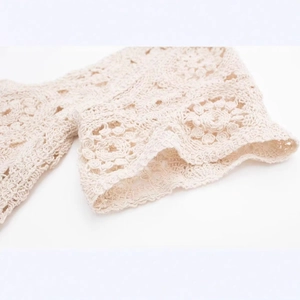 Detailliertes cremefarbenes Häkeloberteil mit eleganten floralen Strickmustern und Wellensaum
