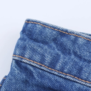 Detailed close-up of blue denim high-waist jeans showing orange stitching and twill fabric