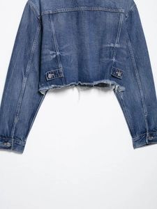 Detailed macro view of cropped denim jacket featuring raw frayed hem and metal buckles