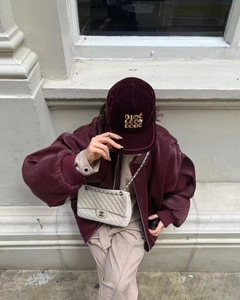 Detail of burgundy pleated texture bomber jacket paired with a luxury quilted chain bag
