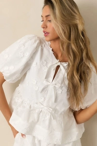 Detail of white puff sleeve top with floral hollow embroidery and delicate bow ties