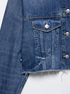 Detailed close-up of blue denim jacket showing twill texture and frayed tassel hemline