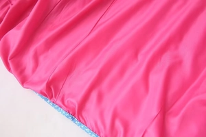 Detail of pink silky fabric with glossy texture and floral print piping on the garment edge