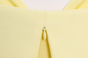 Detail of invisible zipper closure on light yellow puff hem top with smooth fabric texture
