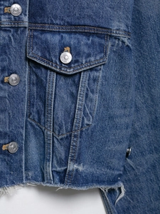 Detail of dark blue denim jacket featuring branded metal buttons and frayed hem edge