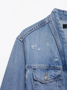 Close-up of light blue denim jacket featuring distressed ripped details and metal buttons