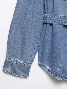 Close-up of light blue washed denim jacket with distressed ripped edges and fringe detail