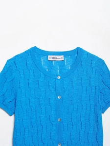 Detail of blue cable knit cardigan featuring round neck, white buttons and brand label