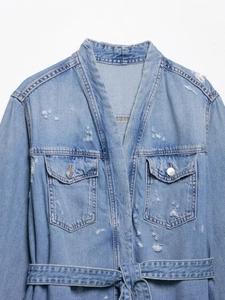 Detail of light blue distressed denim jacket showing cargo pockets and belted waist