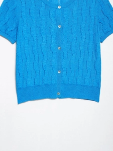 Detailed texture of royal blue knit cardigan with cable pattern and pearl buttons