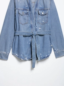 Detailed view of light blue denim jacket with distressed ripped holes and a matching waist belt